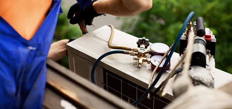 A technician is adjusting an air conditioner with a screwdriver.