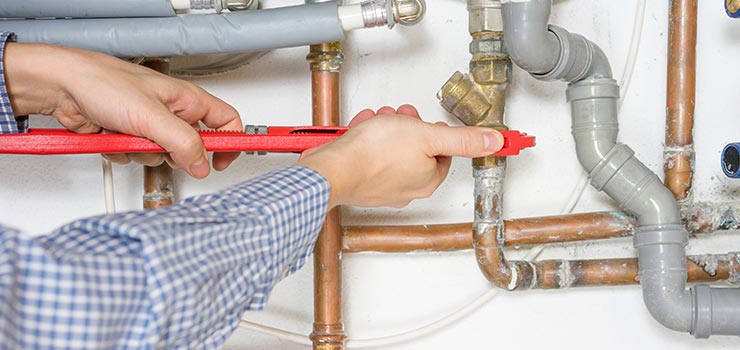 A technician is fixing a pipe with a pipe wrench.