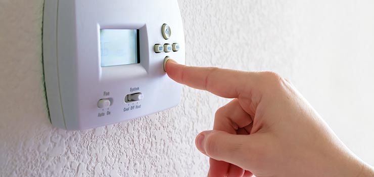 A person is pushing a button on a thermostat to adjust the heating level.